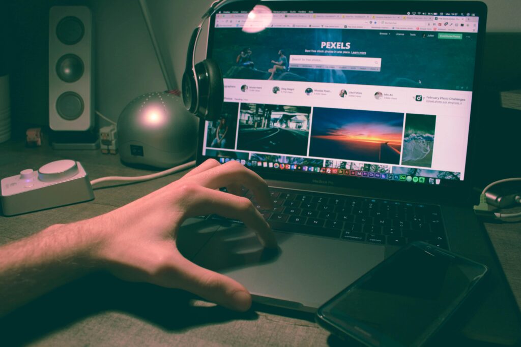 Person browsing Pexels on a laptop with headphones and smartphone nearby.